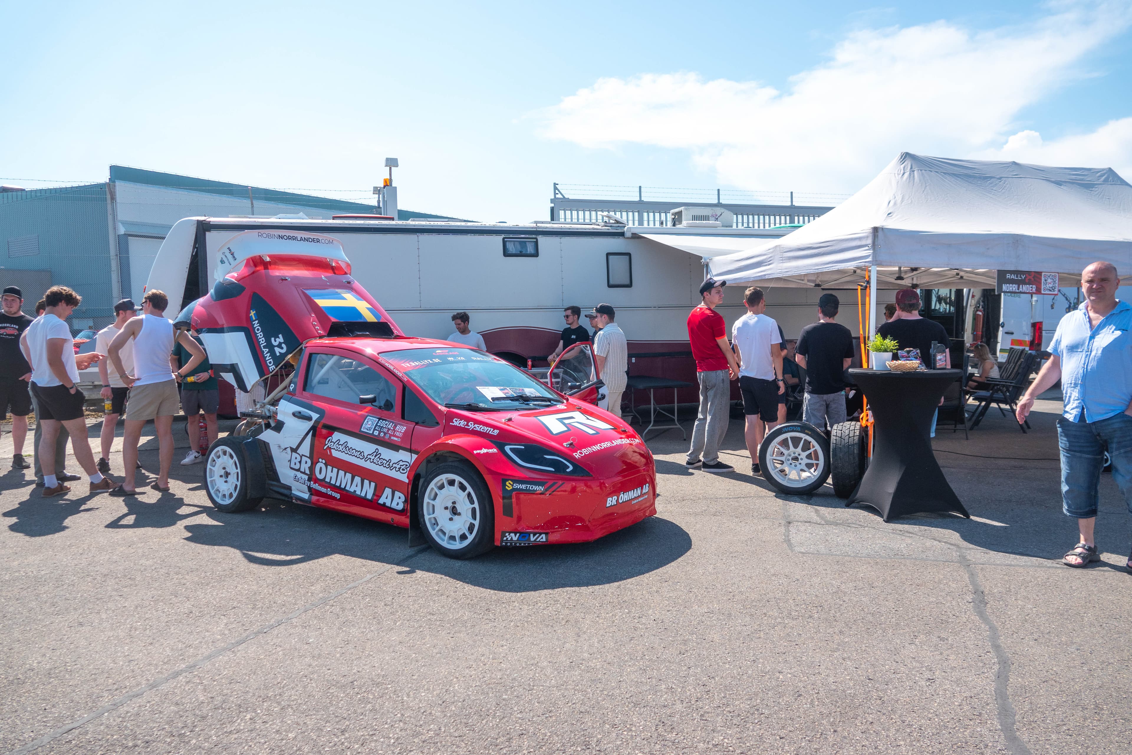 Supercar Lites rallycrossbil i paddocken med öppen huv och publik